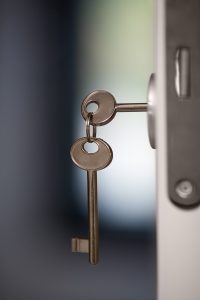 Un par de llaves, una llave está dentro de la cerradura de la puerta y la otra está colgando del aro que las une. Es un ejemplo de la autenticación de dos pasos.